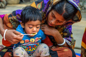 A mother feeds her child at a courtyard feeding session, led by a nutrition facilitator from World Vision's Nobo Jatra program in southwest Bangladesh. The program, which is funded by U.S. foreign assistance, hopes to end the high rate malnutrition for women and children in the area. ©World Vision 2019, Jon Warren.